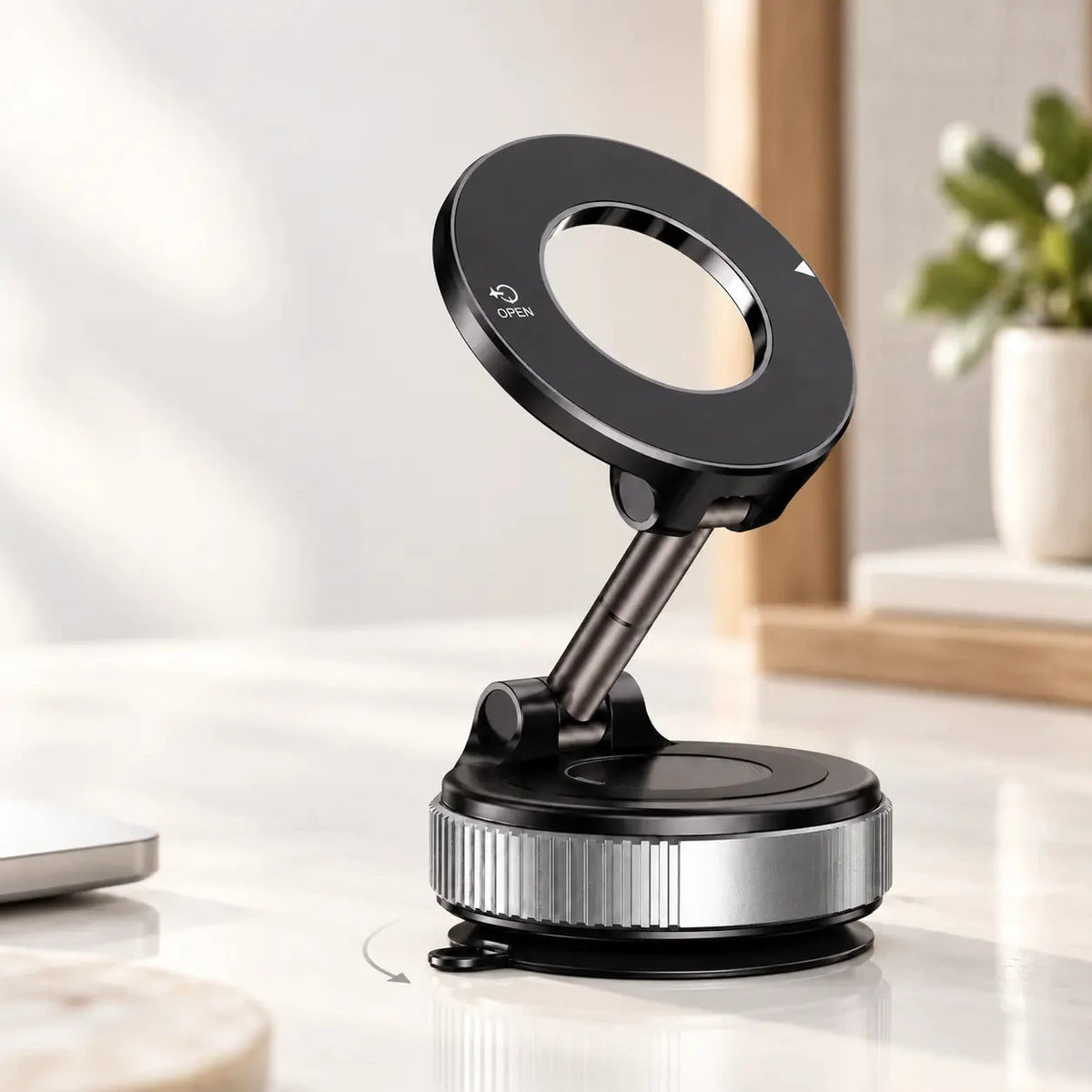 Black and silver suction phone mount standing on a desk with its magnetic head tilted upward.